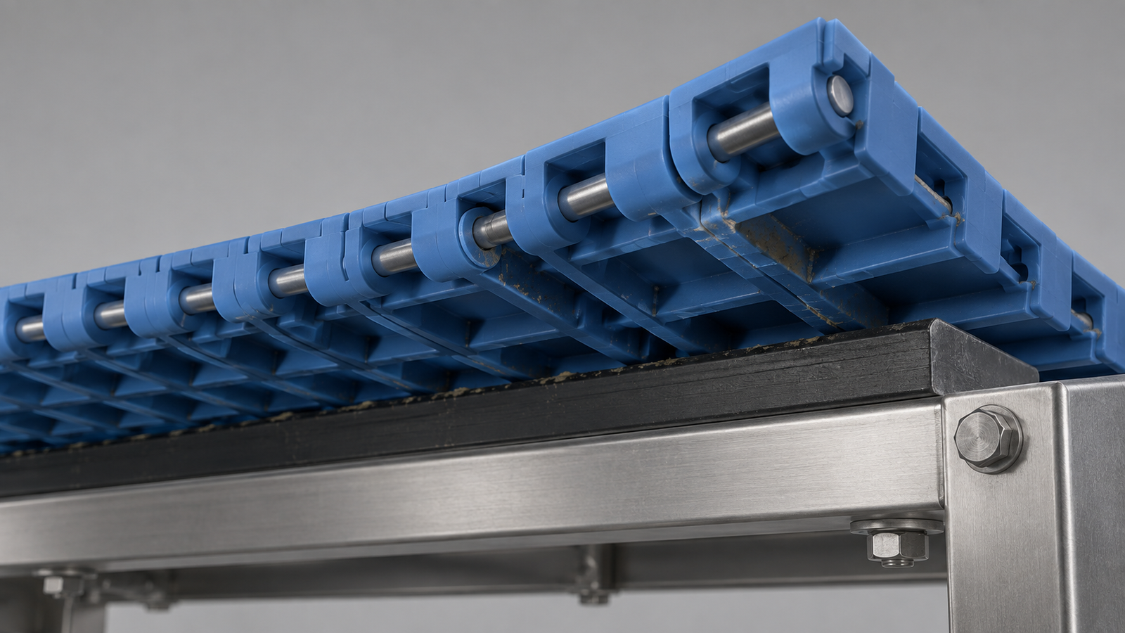 Low underside view of a conceptual modular belt showing hinge pins, ribs and residue near a wear-support contact.